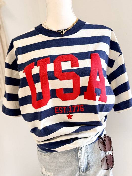 Mannequin wearing a striped sweater with 'USA' and 'EST. 1776' text on a plain background