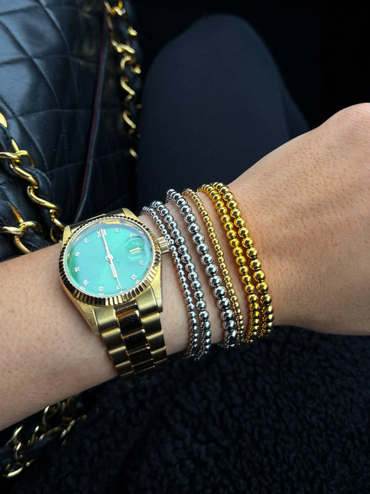 Hand wearing a gold watch and bracelets with a black quilted handbag in the background
